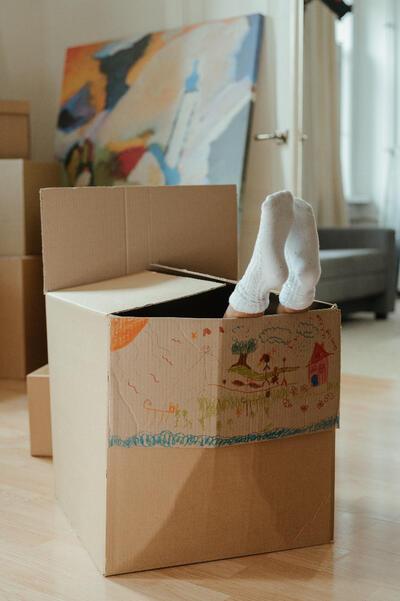 Meisje zit in een verhuisdoos met haar voeten naar boven. Op de doos staat een tekening.